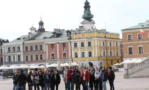 Na zdjęciu grupa uczniów na rynku w Zamościu - w tle kolorowe kamienice.