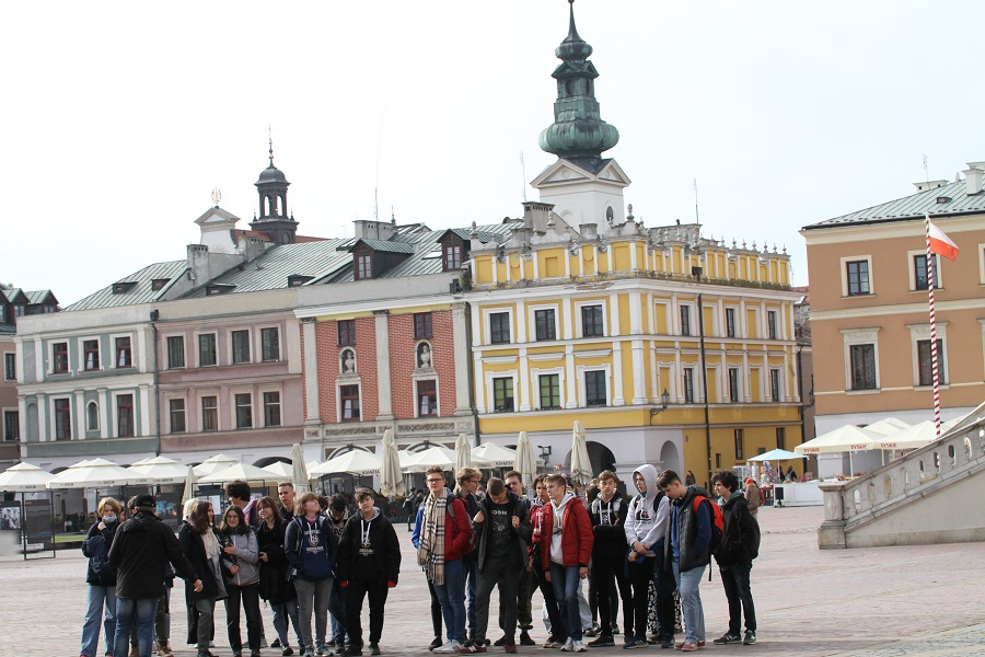 Na zdjęciu grupa uczniów na rynku w Zamościu - w tle kolorowe kamienice.