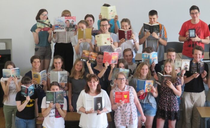 Na zdjęciu kilkunastoosobowa grupa młodzieży i nauczycieli pokazuje okładki czytanych książek.