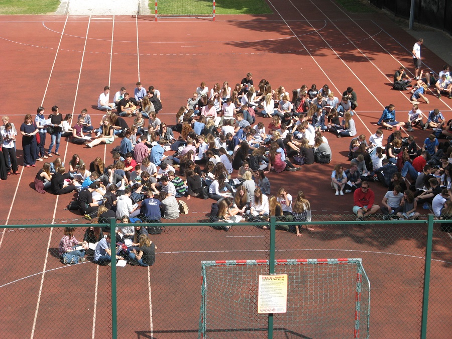 Na zdjęciu uczniowie czytający na szkolnym boisku.