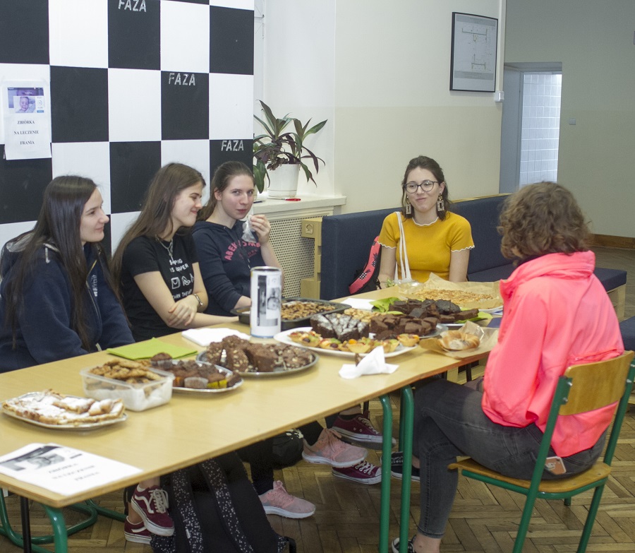 Na zdjęciu grupa młodzieży przy stole zastawionym ciastkami.