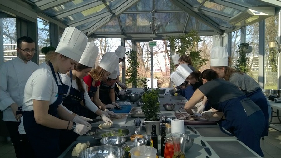 Grupa uczniów w czepkach kucharskich podczas przygotowania posiłku.