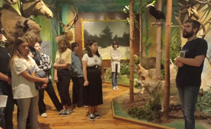 Na zdjęciu uczniowie zwiedzający muzeum i słuchający przewodnika.