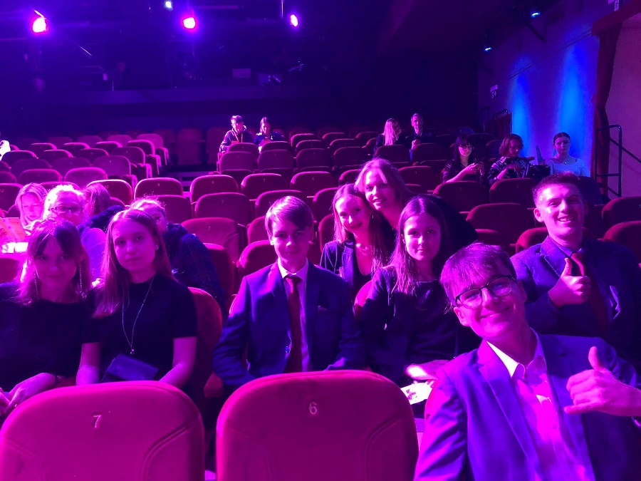 Na zdjęciu grupka młodzieży na widowni teatralnej w fioletowej poświacie.