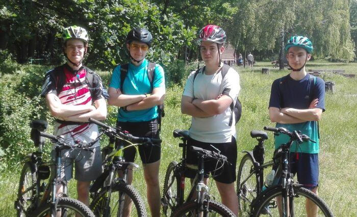 Na zdjęciu czterech młodych rowerzystów w kaskach stoi przy rowerach.