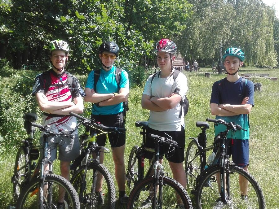 Na zdjęciu czterech młodych rowerzystów w kaskach stoi przy rowerach.