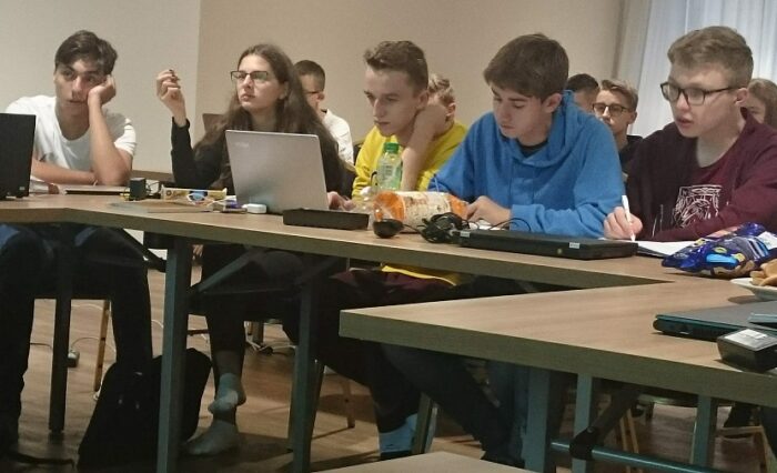 Na zdjęciu grupa młodzieży przy laptopach.