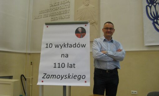 Na zdjęciu wykładowca stoi przy tablicy z napisem "10 wykładów na 110 lat Zamoyskiego".