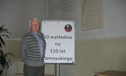 Na zdjęciu wykładowca stoi przy tablicy z napisem "10 wykładów na 110 lat Zamoyskiego".