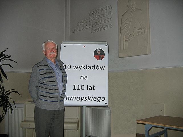 Na zdjęciu wykładowca stoi przy tablicy z napisem "10 wykładów na 110 lat Zamoyskiego".
