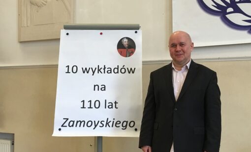 Na zdjęciu wykładowca stoi przy tablicy z napisem "10 wykładów na 110 lat Zamoyskiego".