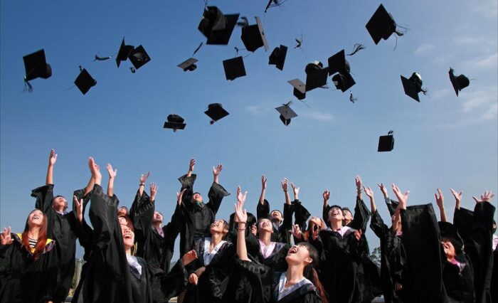 Na zdjęciu studenci w czarnych togach podrzucający do góry swe czapki.