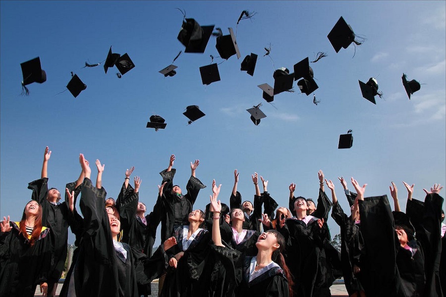 Na zdjęciu studenci w czarnych togach podrzucający do góry swe czapki.