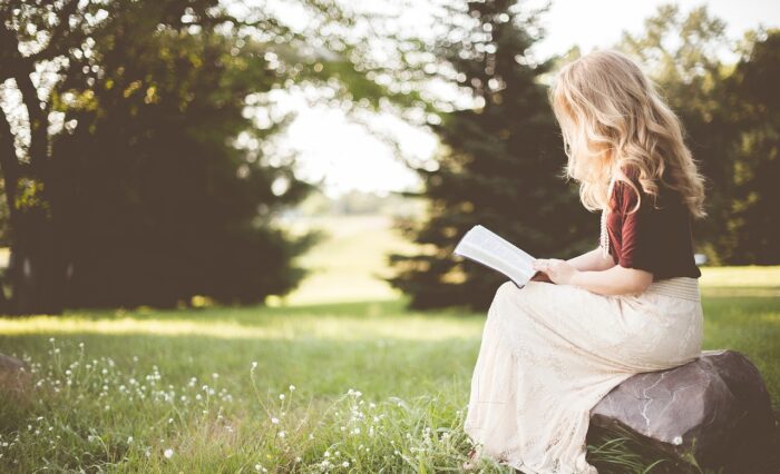 Na zdjęciu siedząca dziewczyna czytająca na łonie natury.