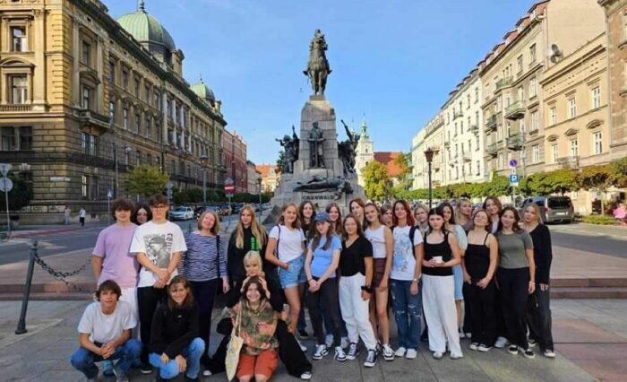 Na zdjęciu duża grupa młodzieży pozuje pod pomnikiem.