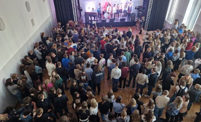 Na zdjęciu artyści na scenie i społeczność szkolna zgromadzona w auli na koncercie.