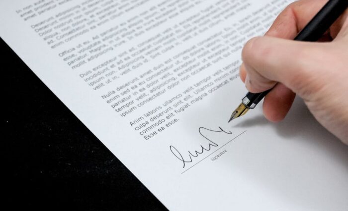 Na zdjęciu fragment dłoni z długopisem podczas składania podpisu.